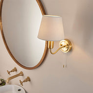 Wall-mounted lamp with a white shade and gold fixture next to a round mirror in a bathroom setting. Conway Brushed Satin Gold Wall Light, bathroom wall light, LHEND93852, wall light,